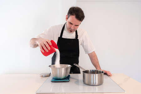 Hands of a man cooking a red velvet cake at home, preparing Swiss meringue with egg whites in a bain-marie, adding sugar, work at homeの写真素材