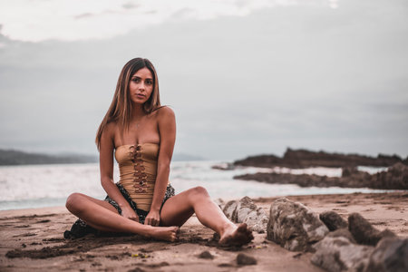 Portrait of a brunette woman wearing a swimsuit and a pareo on the beach in summer, sitting on the sandの写真素材