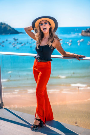 Blonde woman in a luxury hotel on a terrace wearing a hat with sunglasses and the sea in the backgroundの写真素材