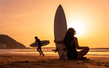 Silhouette of a surfer woman on a beach at sunset with the surfboardの写真素材