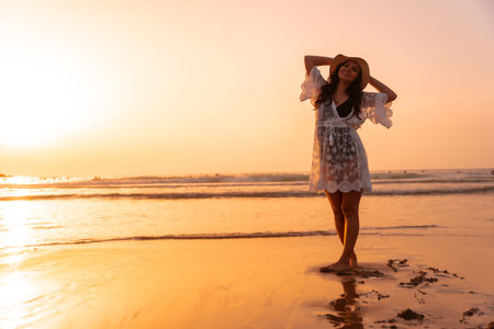 A woman in the sunset in a white dress at the sea in summer with a hatの写真素材