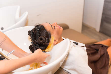 Hairdresser applying a blonde dye to a female client, cleaning her hairの写真素材