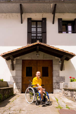 Portrait of a disabled person dressed in yellow in a wheelchair in the entrance of his house smilingの写真素材
