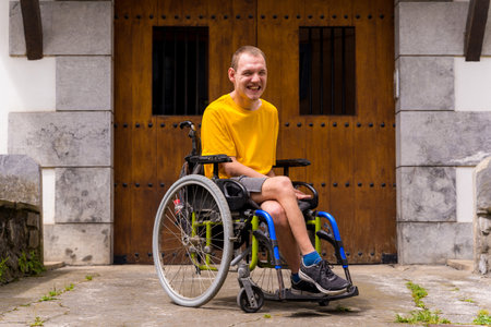 Portrait of a disabled person dressed in yellow in a wheelchair in the entrance of his house smilingの写真素材