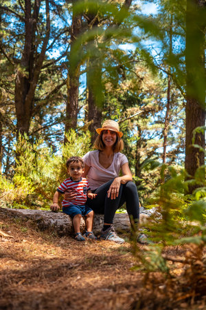 Portrait of a mother with her son sitting on a tree in nature next to pine trees, Madeira. Portugalの写真素材