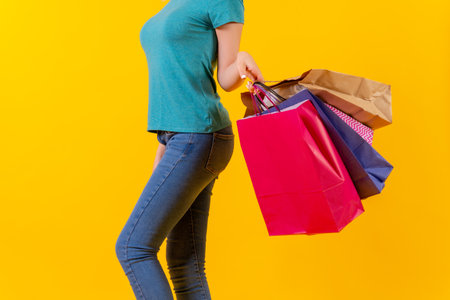 Unrecognizable person with colored shopping bags on discounts, yellow background studioの写真素材