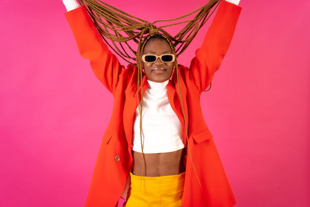 Black ethnic woman with braids on a pink background, portrait in a red suit and yellow pants