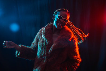 Black ethnic woman with braids with blue and red led lights, model having fun and dancingの写真素材