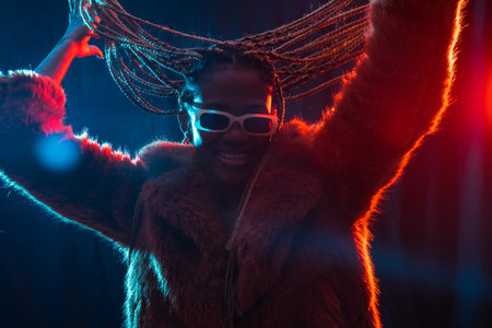 Black ethnic woman with braids with blue and red led lights, having fun and dancing at partyの写真素材