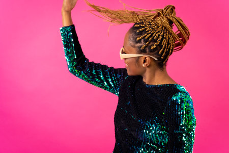 African young woman with party braids on a pink background, smiling dancing and looking