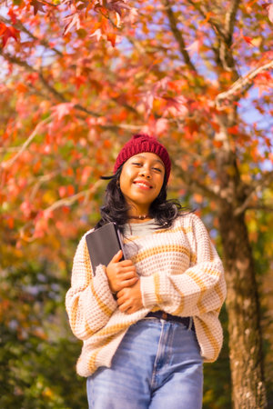 Portrait of asian girl in autumn with a tablet smiling in a forest of red leaves, technology concept