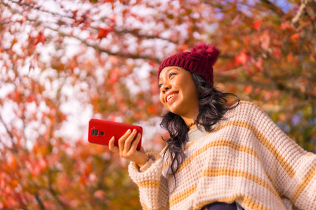 Portrait of an Asian woman in autumn with a mobile sending a voice message in a forest of red...