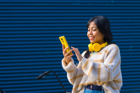 Asian girl choosing the music on the phone to listen on a blue college backgroundの写真素材