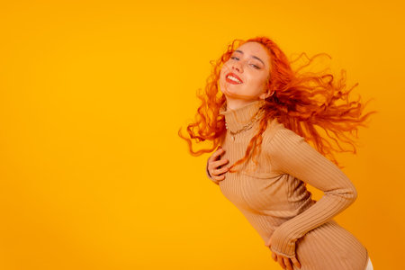 Red-haired woman on a yellow background, studio shot, moving her hair, tousled hairの写真素材