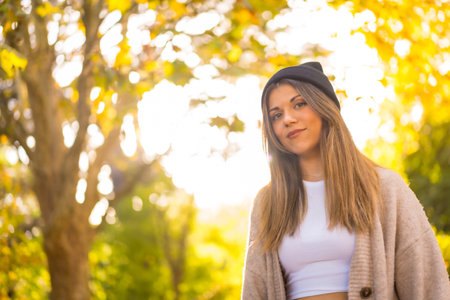 Portrait of a young blonde girl in a woolen hat in autumn, walking in the park at sunsetの写真素材