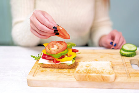 Unrecognizable person cooking a vegetable sandwich in the kitchen at home. Preparing it by putting tomatoの写真素材