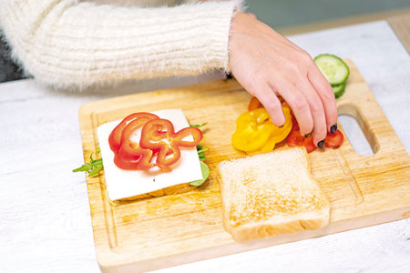 Unrecognizable person cooking a vegetable sandwich in the kitchen at home. Placing the red pepperの写真素材
