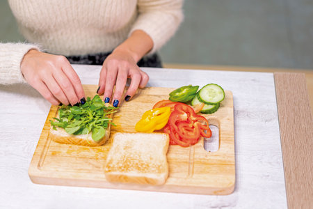 Unrecognizable person cooking a vegetable sandwich in the kitchen at home. Placing the arugulaの写真素材