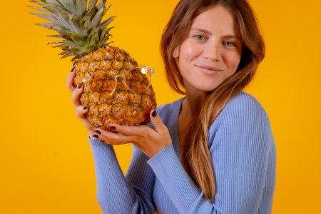 Woman smiling with a pineapple in sunglasses in a studio on a yellow background, healthy, summerの写真素材