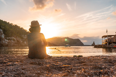 A young woman sitting looking at Benirras beach in Ibiza at sunset. holiday conceptの写真素材