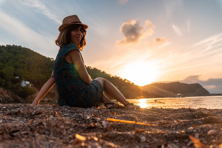 A young woman sitting on the beach looking at the sunset of Benirras in Ibiza. holiday conceptの写真素材