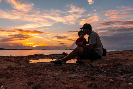 Sunset in Ibiza on vacation, young father giving his son a kiss by the sea, San Antonio Abadの写真素材