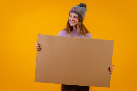 Woman in a wool cap holding a cardboard sign on a yellow backgroundの写真素材