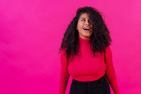 Curly-haired woman smiling on a pink background, studio shot, lifestyle