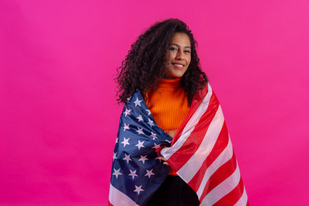 Curly-haired woman embracing usa flag on a pink background, studio shotの写真素材