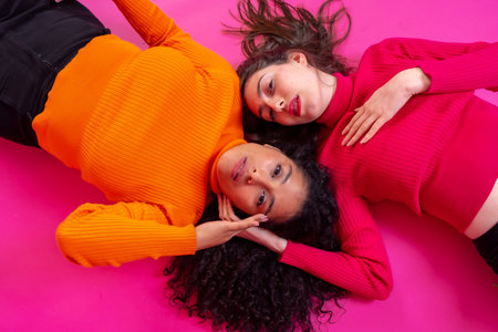 Two multi-ethnic women lying in a trendy posing on a pink background, lifestyleの写真素材