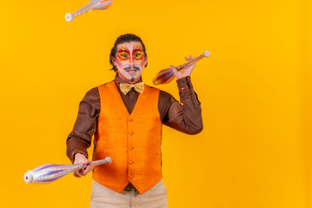 Happy juggler man in makeup vest juggling maces on a yellow backgroundの写真素材