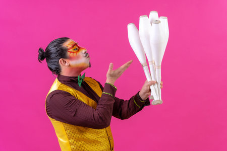 Juggler in a vest and with painted face juggling maces on a pink background, blowing kissesの写真素材