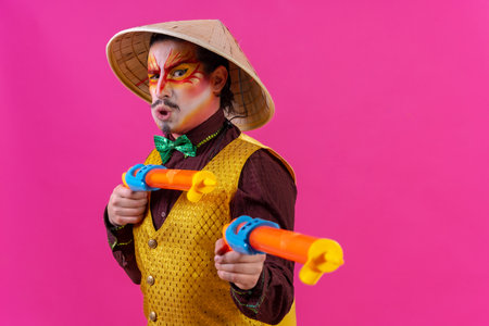 Clown with white facial makeup on a pink background, with toy guns and a Chinese hatの写真素材