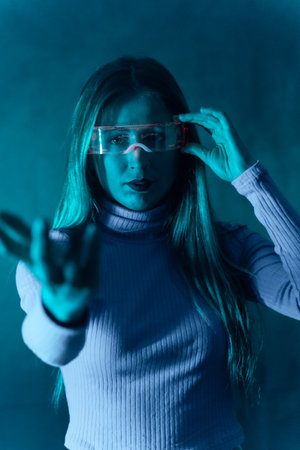 Blonde woman with futuristic glasses gesturing against a blue backgroundの写真素材