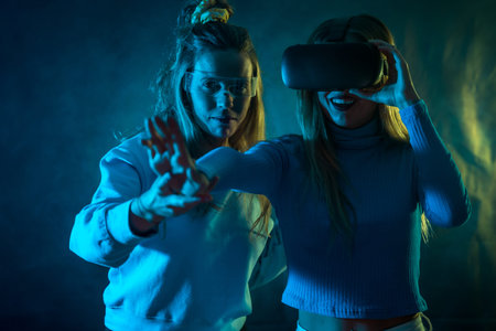 Two futuristic women in vr glasses, looking at the metaverse, blue background