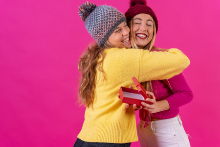 Two young blonde caucasian women hugging the friend thanking her for the gift, isolated on a pink backgroundの写真素材
