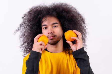 Portrait with orange fruit and smiling. Young boy with afro hair on white background