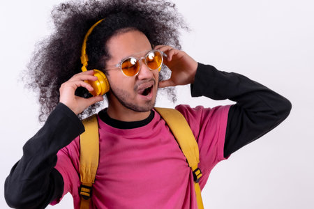 Portrait with pink t-shirt and backpack listening to music. Young man with afro hair on white...