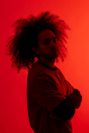 Silhouette in red light with arms crossed. Young man with afro hair on white backgroundの写真素材