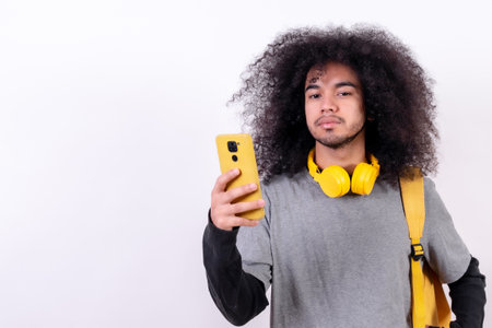Young college boy with afro hair on white background, listening to musicの写真素材
