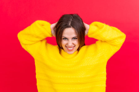 Close up portrait of young woman, cheerful isolated on red studio background in yellow woolen pulloverの写真素材