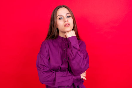 Close up portrait of young caucasian woman in purple shirt isolated on red background, looking at cameraの写真素材