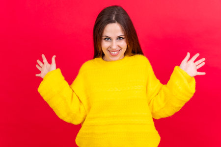Close up portrait of young woman, cheerful isolated on red studio background in yellow woolen pulloverの写真素材