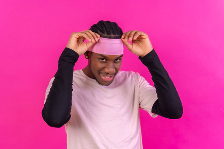 Black ethnic man in pink clothes on a pink background, concept portrait, putting on the headbandの写真素材