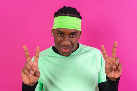 Black ethnic man in green clothes on a pink background, making the win gesture