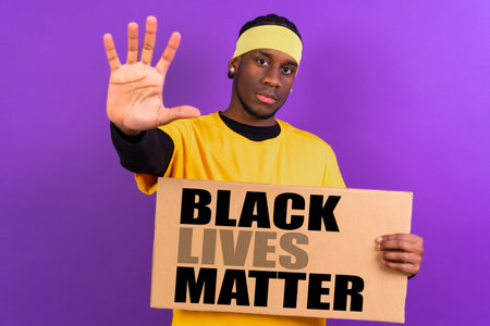 Black ethnic man in yellow clothes on a purple background, pointing holding a sign, black lives matter, making stop with his handの写真素材