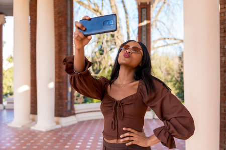 A beautiful natural young African woman in a park. Smiling with sunglasses taking a selfie, lifestyleの写真素材