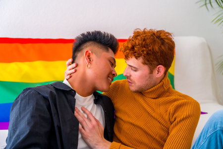 Beautiful gay couple being romantic at home by the sofa kissing, lgbt concept, rainbow flagの写真素材