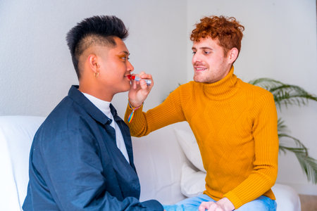 Beautiful gay couple putting on makeup painting their lips, being romantic indoors at home, lgbt conceptの写真素材