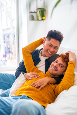 Beautiful gay couple being romantic at home on the sofa, portrait cuddling, lgbt conceptの写真素材